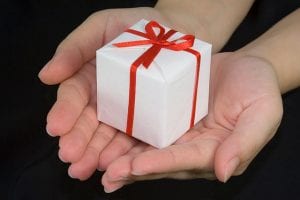 two hands handing a small white gift wrapped box with a red bow